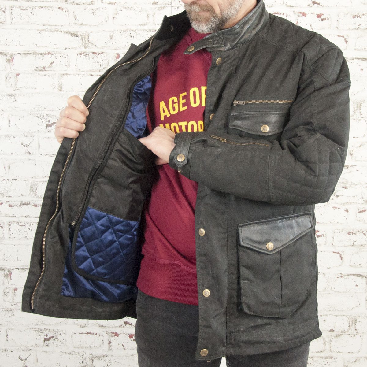 man with a beard wearing an Age of Glory protective motorbike jacket that has a blue satin lining and is brown waxed cotton featuring bronze zips.